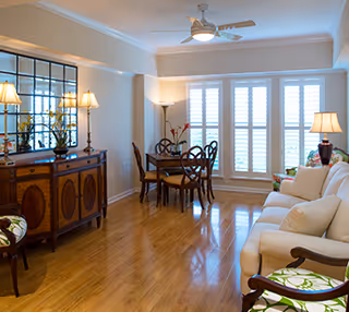 Bright combined living and dining area with hardwood floors, a sofa and chairs, a dining table, a sideboard with mirror, and shuttered windows.
