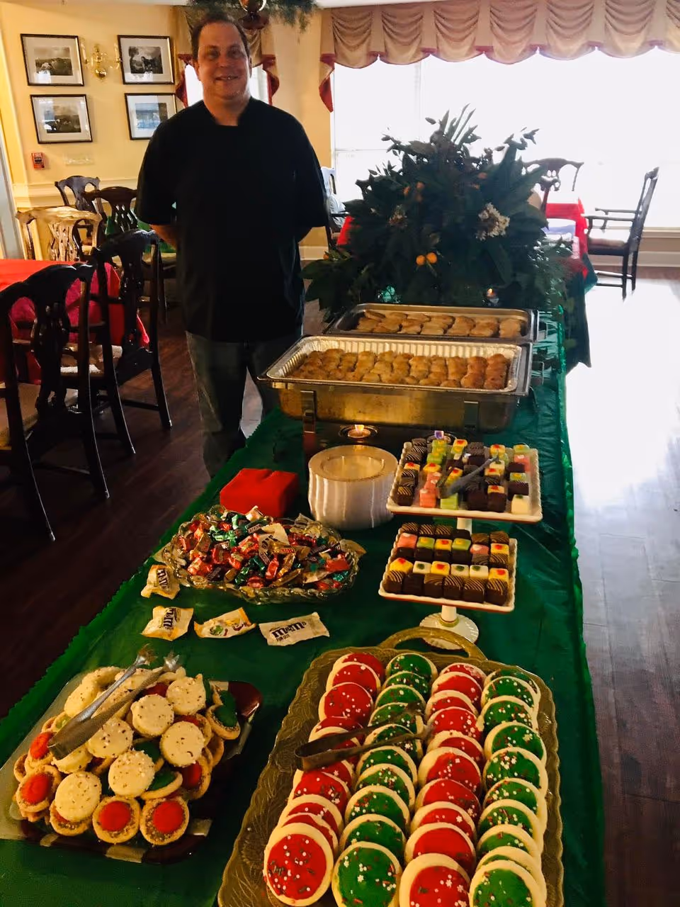Buffet table laid out with trays of cookies, candies and desserts in a dining room with a staff member standing at the far end.