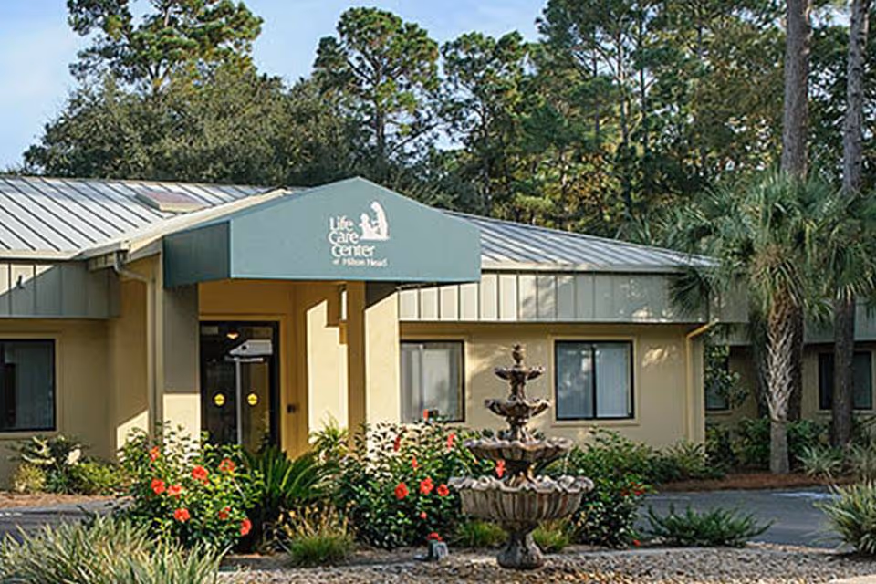 Front entrance of Life Care Center of Hilton Head with a green canopy, fountain, and landscaped plants.