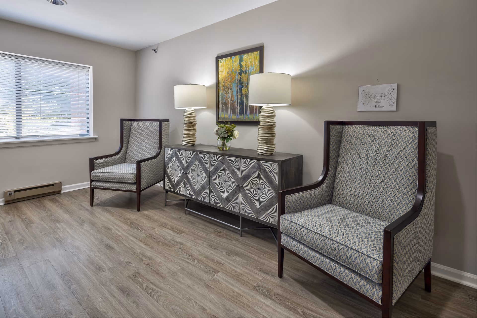 Two upholstered armchairs flank a decorative console table with lamps and artwork in a small sitting area.