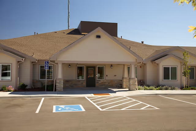 Front entrance of a single-story building with a covered porch, stone pillars, and marked accessible parking spaces.