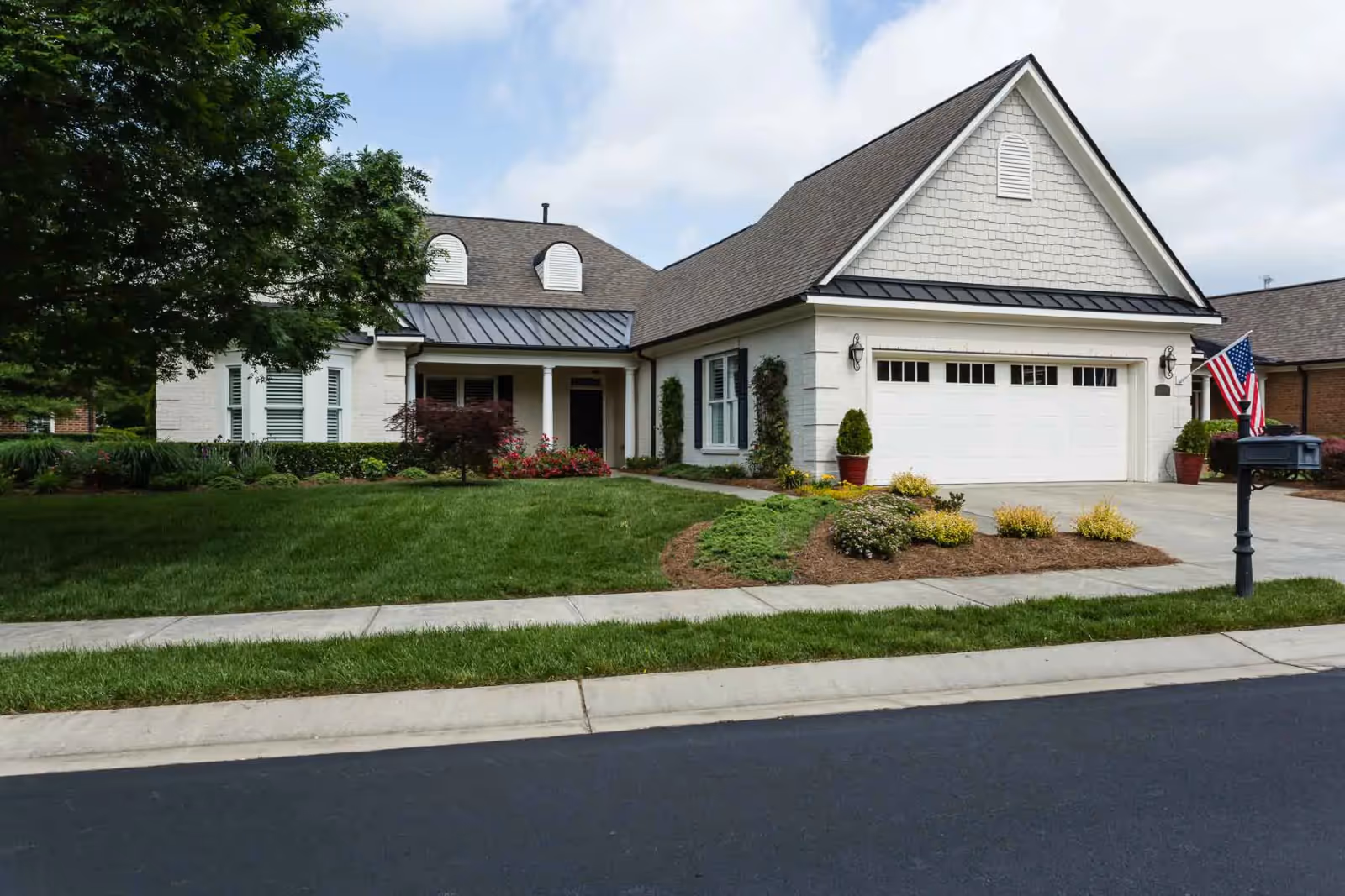 Front exterior of a single-story suburban house with a two-car garage, manicured lawn, and an American flag by the driveway.