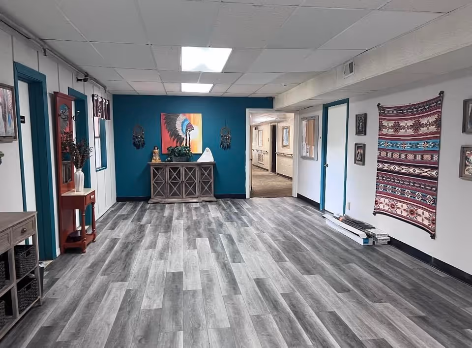 Spacious interior common area with gray wood-look flooring, a teal accent wall with a console table and artwork, and decorative textiles on the opposite wall.