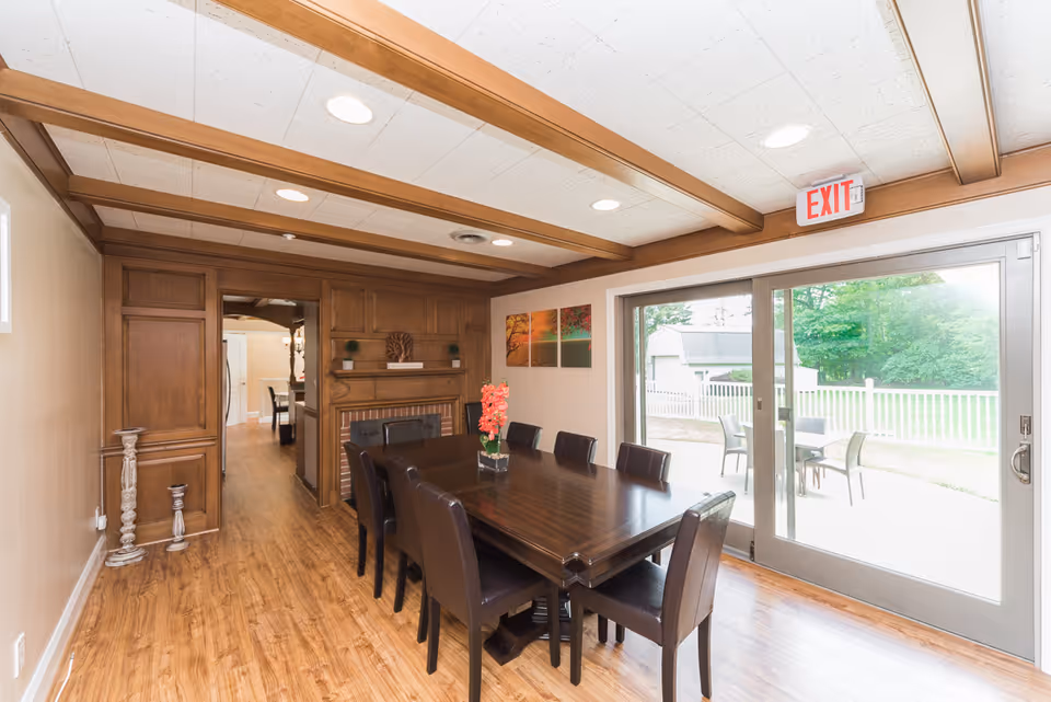 Bright dining room with a long wooden table and chairs, wood-paneled ceiling and sliding glass doors opening to an outdoor patio.