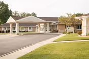 Front exterior of a single-story senior living facility with a covered drive-up entrance and landscaped lawn.