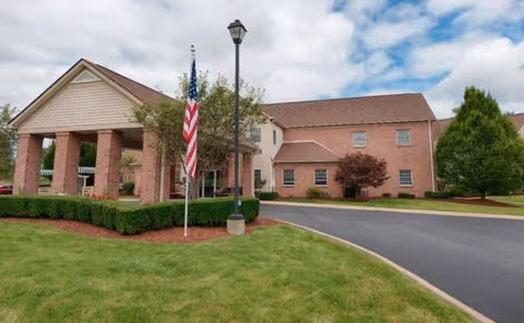 Brick senior living facility exterior with flag, driveway, and manicured landscaping.