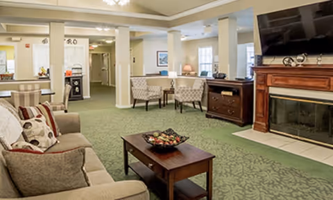 Communal living room with sofas, armchairs, a coffee table, fireplace and wall-mounted TV.