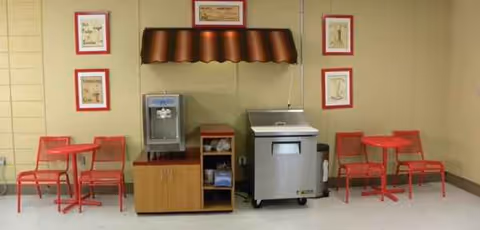 Red tables and chairs line a beige wall with a beverage machine and an ice dispenser.