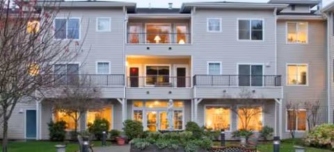 Exterior view of Brookdale Stanwood: a three-story senior living building with balconies and lit windows.