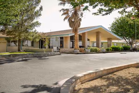 Front exterior of Rimrock Villa Convalescent Hospital with entrance, driveway, and palm trees.