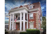 Front exterior view of Elizabeth Brewster House, a large brick building with white columns, an American flag, and a sign displaying the facility's name above the entrance.