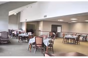 Spacious dining room with multiple tables covered in white tablecloths and wooden chairs beneath a high vaulted ceiling.