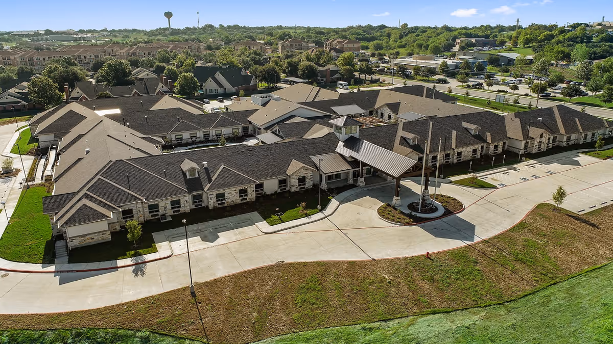Aerial view of a single‑story senior living complex with a circular drive and covered main entrance surrounded by lawns and parking.