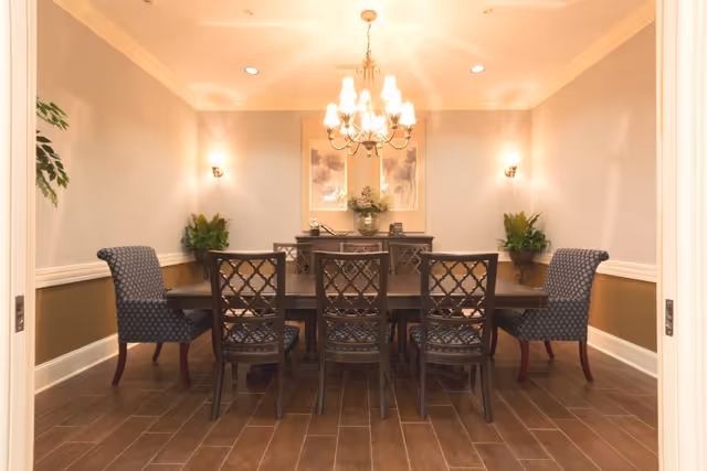 Formal dining room with a large wooden table, upholstered chairs, a chandelier, and wall decor.
