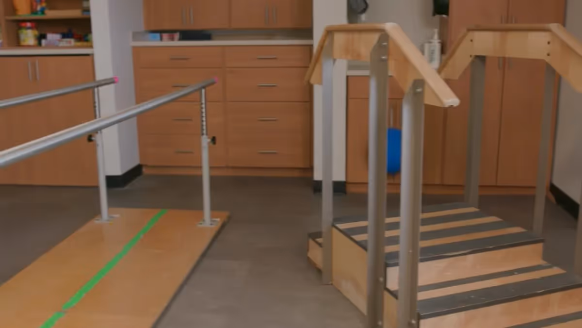 Interior view of a therapy area featuring parallel bars and a small staircase for rehabilitation exercises.