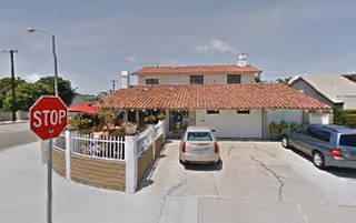 Exterior of a single-story facility with a red tile roof, driveway, and parked cars.