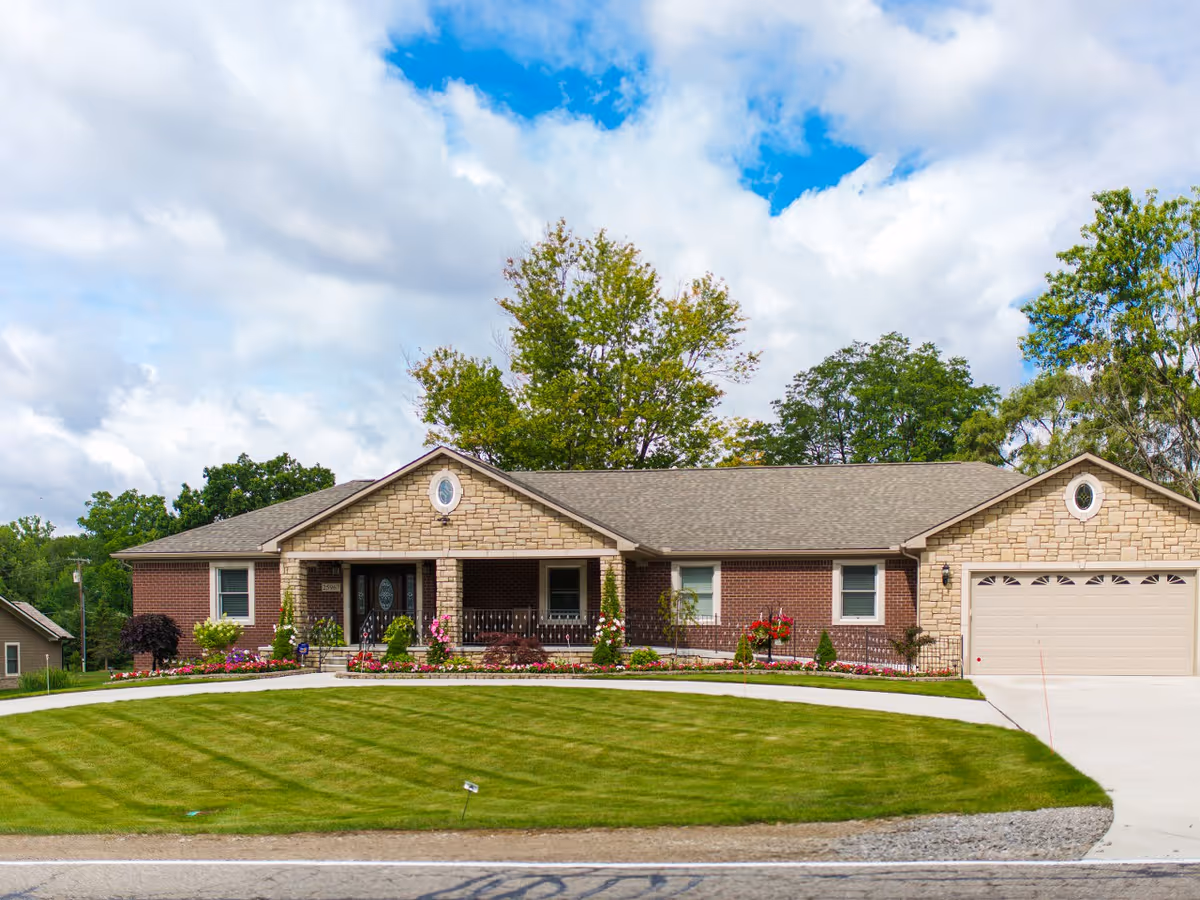 Front exterior view of a single-story brick and stone building with a well-maintained lawn and flower beds, under a partly cloudy blue sky.