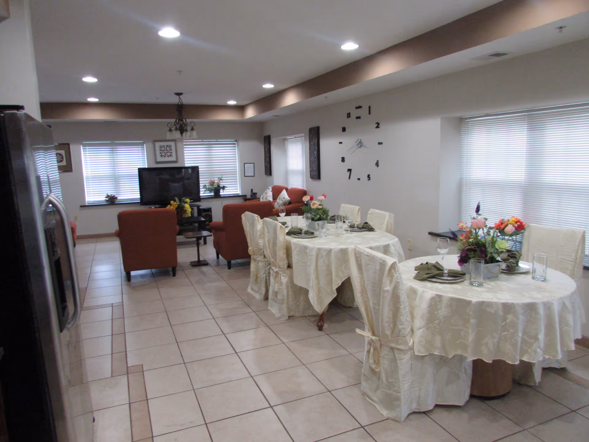 Indoor dining area with two round tables covered in white cloths and red seating.