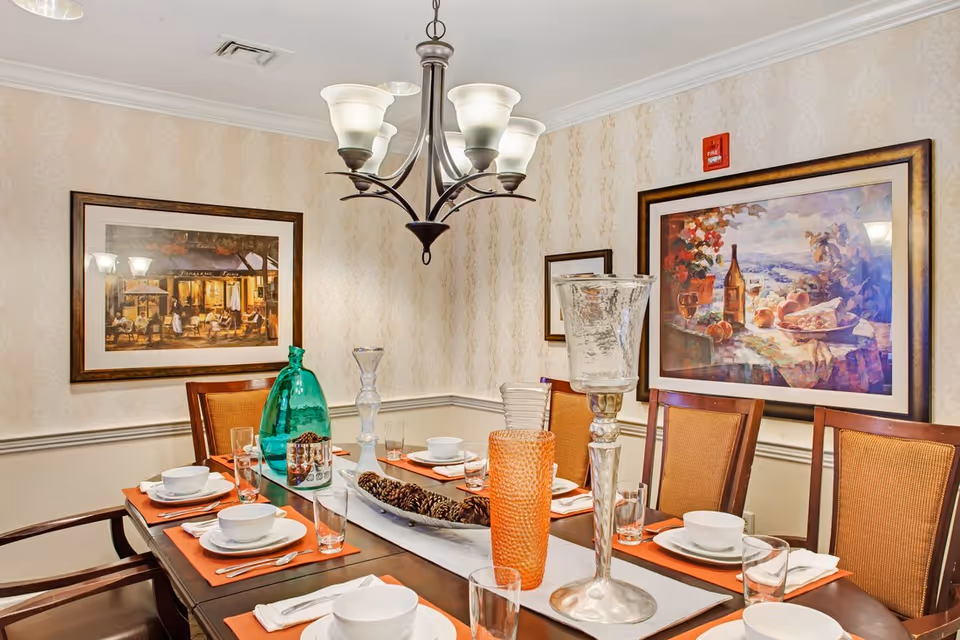 A dining room with a set table, chairs, decorative vases and candles, a chandelier overhead, and framed artwork on the walls.