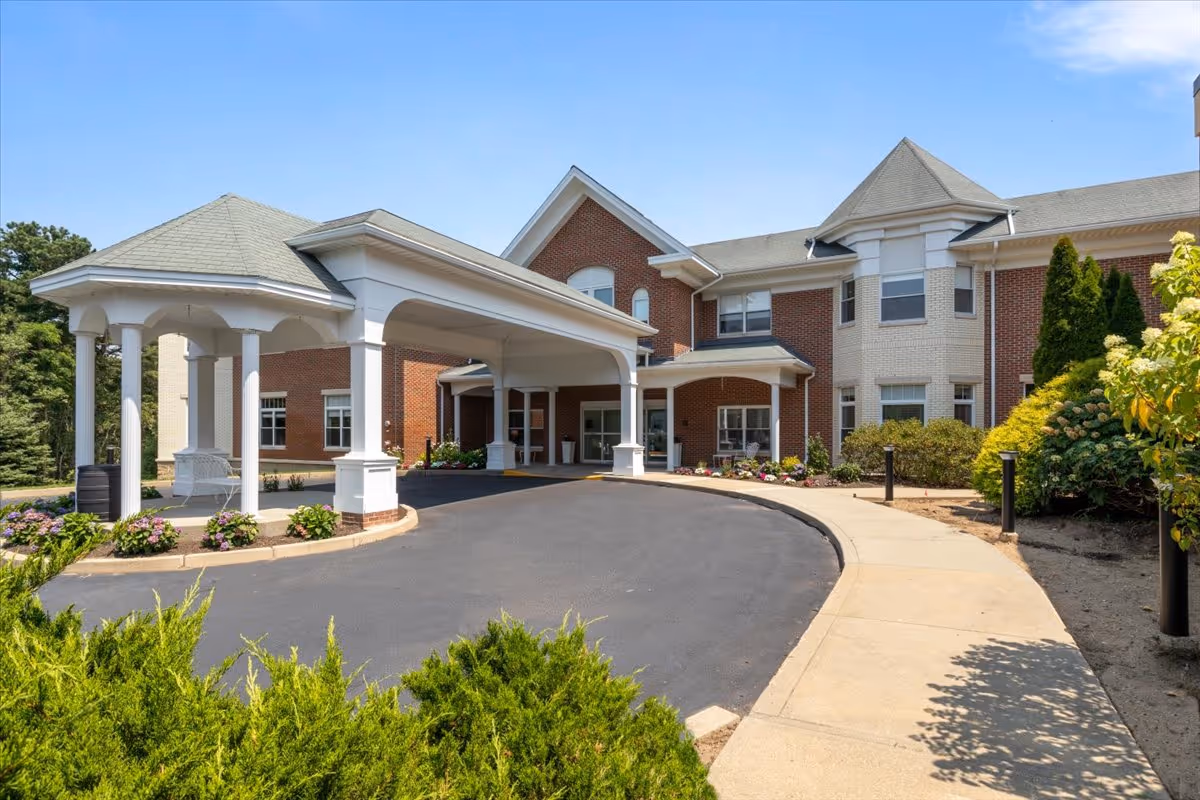 Front entrance of a brick residential building with a covered porte-cochère, circular driveway, and landscaped beds.