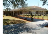 Single-story brick building with a covered entrance and walkway, landscaped shrubs and lawn, and trees in front.