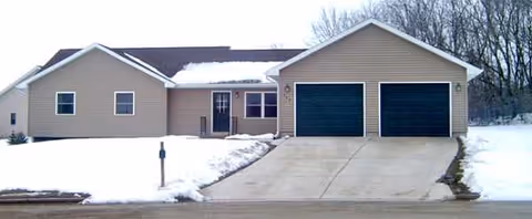Front exterior of a beige, single-story facility with two black garage doors and snow.