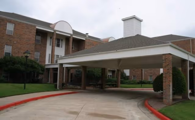 Brick assisted living building with a covered entrance drive and surrounding green landscaping.