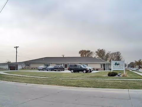 Exterior view of a single-story building with a parking lot in front containing several cars. There is a sign on the lawn that reads Edgewood Vista Norfolk. The sky is overcast and there are some trees in the background.