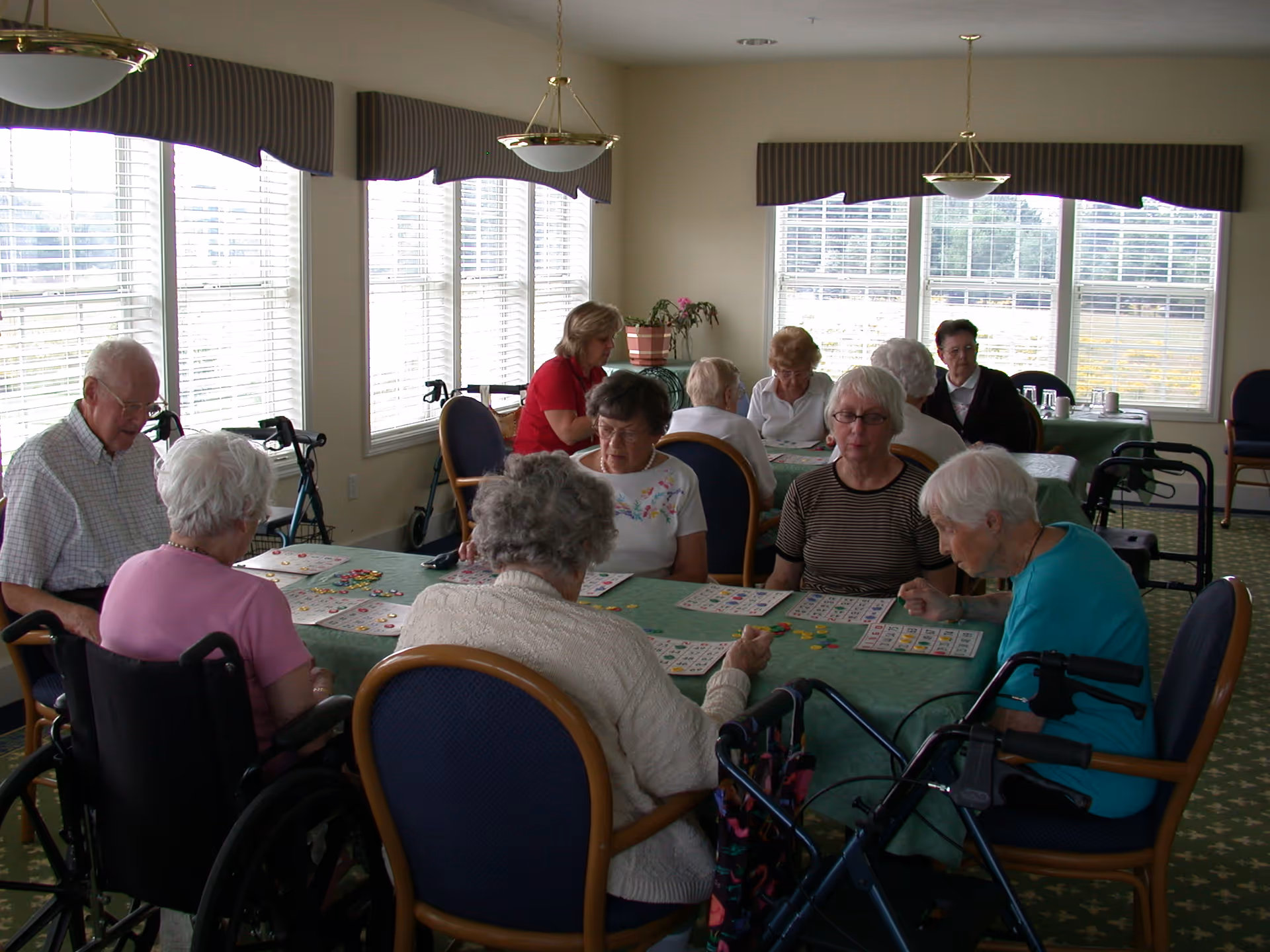 A group of elderly residents sitting around tables playing bingo in a bright community room.
