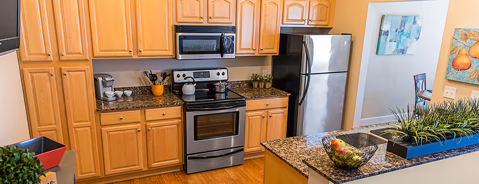 Bright kitchen with wooden cabinets, stainless steel appliances, granite countertops and an island topped with a fruit bowl and planter.