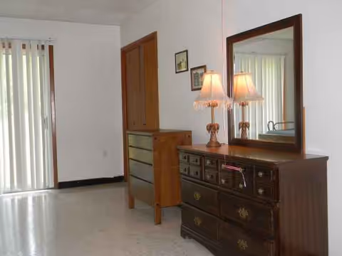 Wood dresser with mirror and two lamps in a bright bedroom corner.