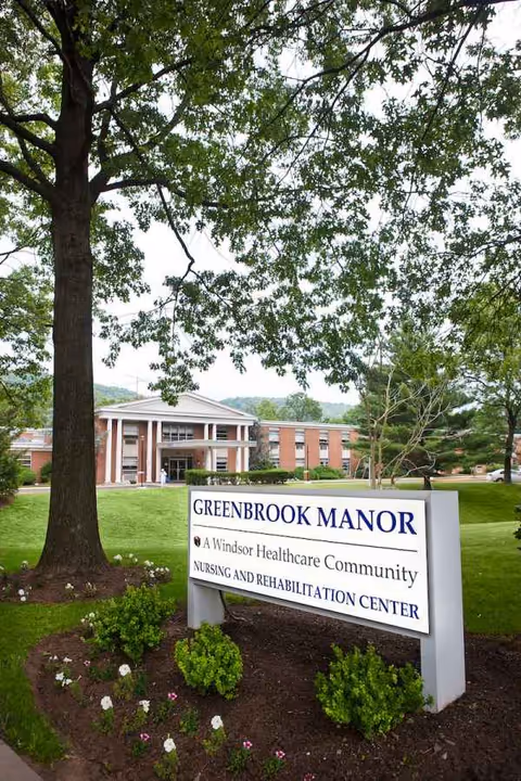 Exterior view of Greenbrook Manor nursing and rehabilitation center with a sign in front
