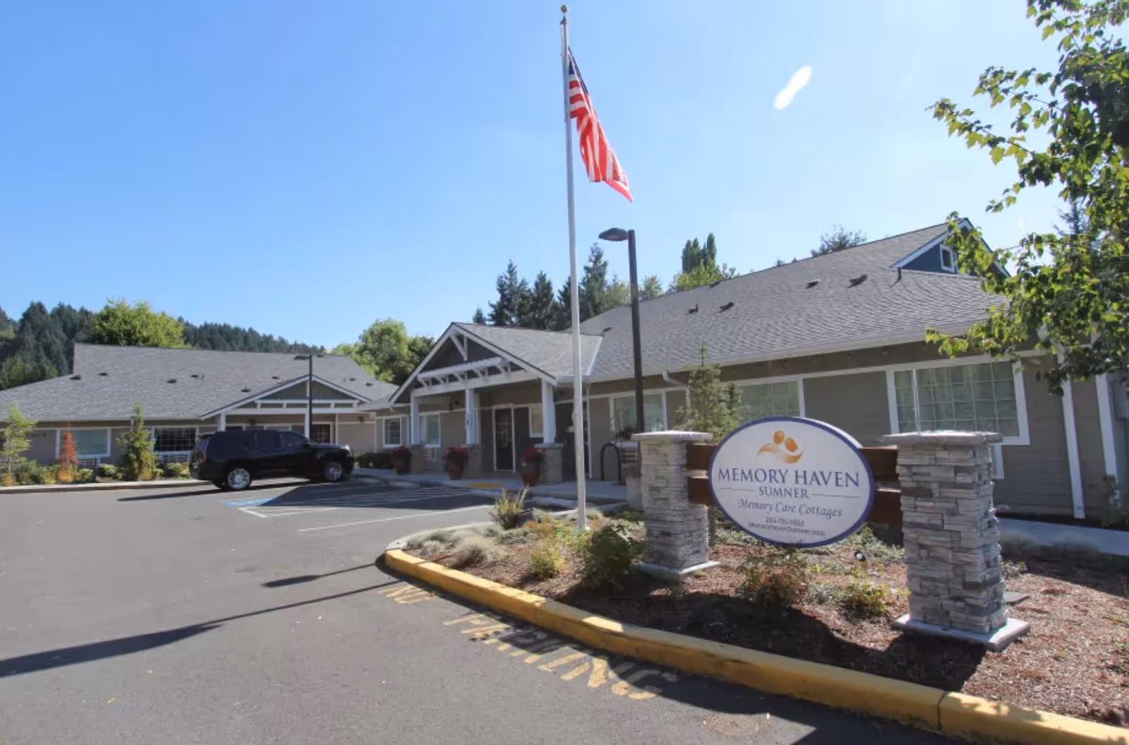 Front exterior of the Memory Haven facility showing the entrance, an American flag, parking area, and a sign reading "Memory Haven".