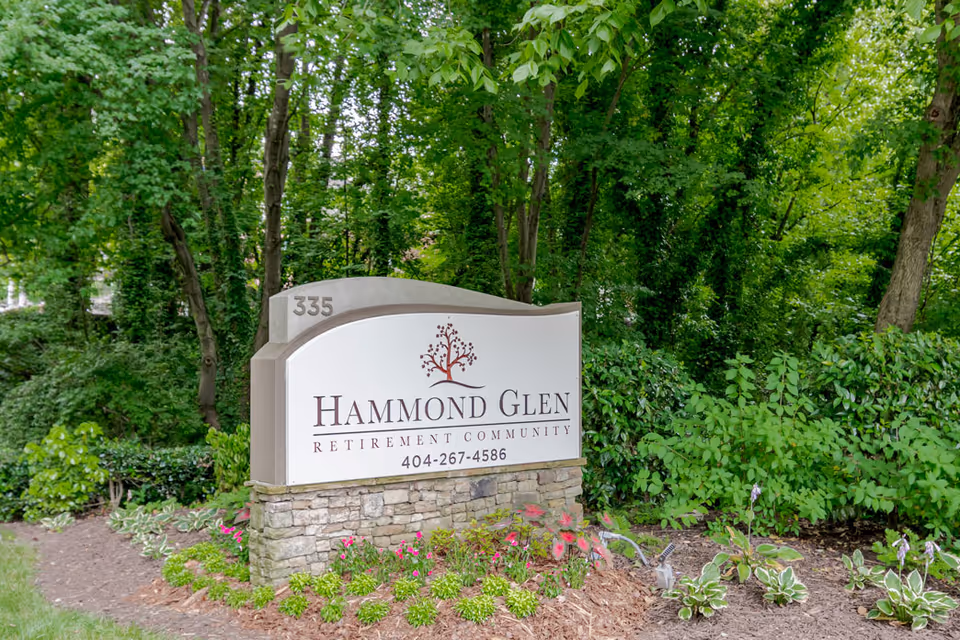 Stone and concrete sign for Hammond Glen Retirement Community with the phone number 404-267-4586, surrounded by green trees and plants.