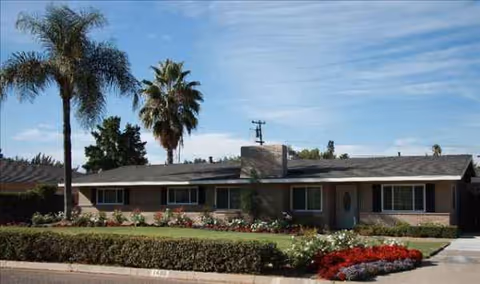 Front exterior of Gift of Grace Care Home, a single-story building with lawn and palm trees.