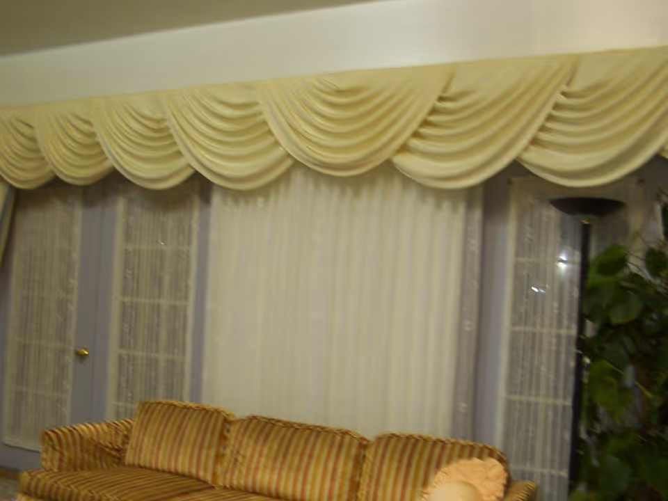 Striped upholstered sofa in front of tall draped curtains with a floor lamp and potted plant in a living room.
