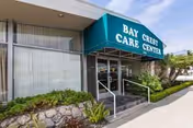Exterior view of Bay Crest Care Center entrance with teal awning and landscaped walkway.