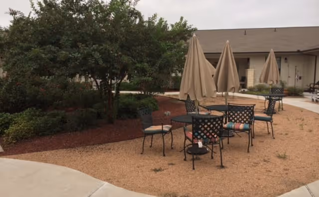 Courtyard with metal patio tables and umbrellas surrounded by landscaping in front of a single-story building.