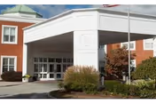 Entrance of Taconic Rehabilitation and Nursing at Hopewell showing a covered drop-off area with white pillars, a brick building facade, and landscaped bushes and plants around the driveway.