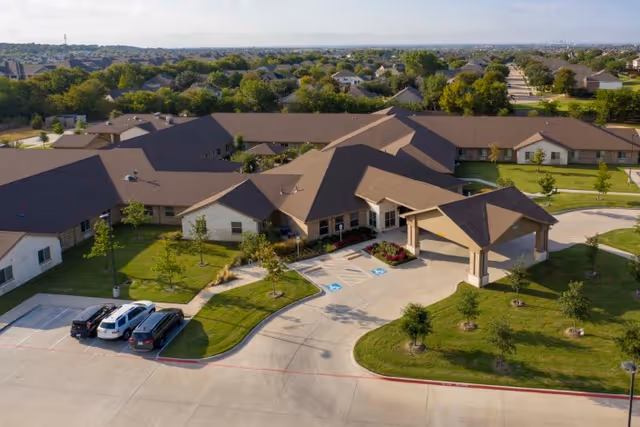 Aerial view of a single-story senior care campus with a covered entrance drive, parking spaces, and landscaped lawns.