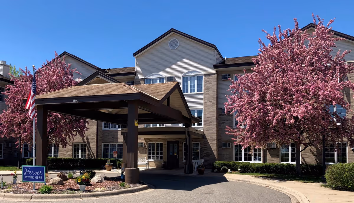 Senior living facility with a covered entrance, pink blossoming trees, and an American flag.
