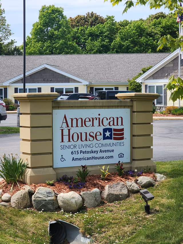 Entrance sign reading "American House Senior Living Communities" in front of a single-story senior living building and landscaped lawn.