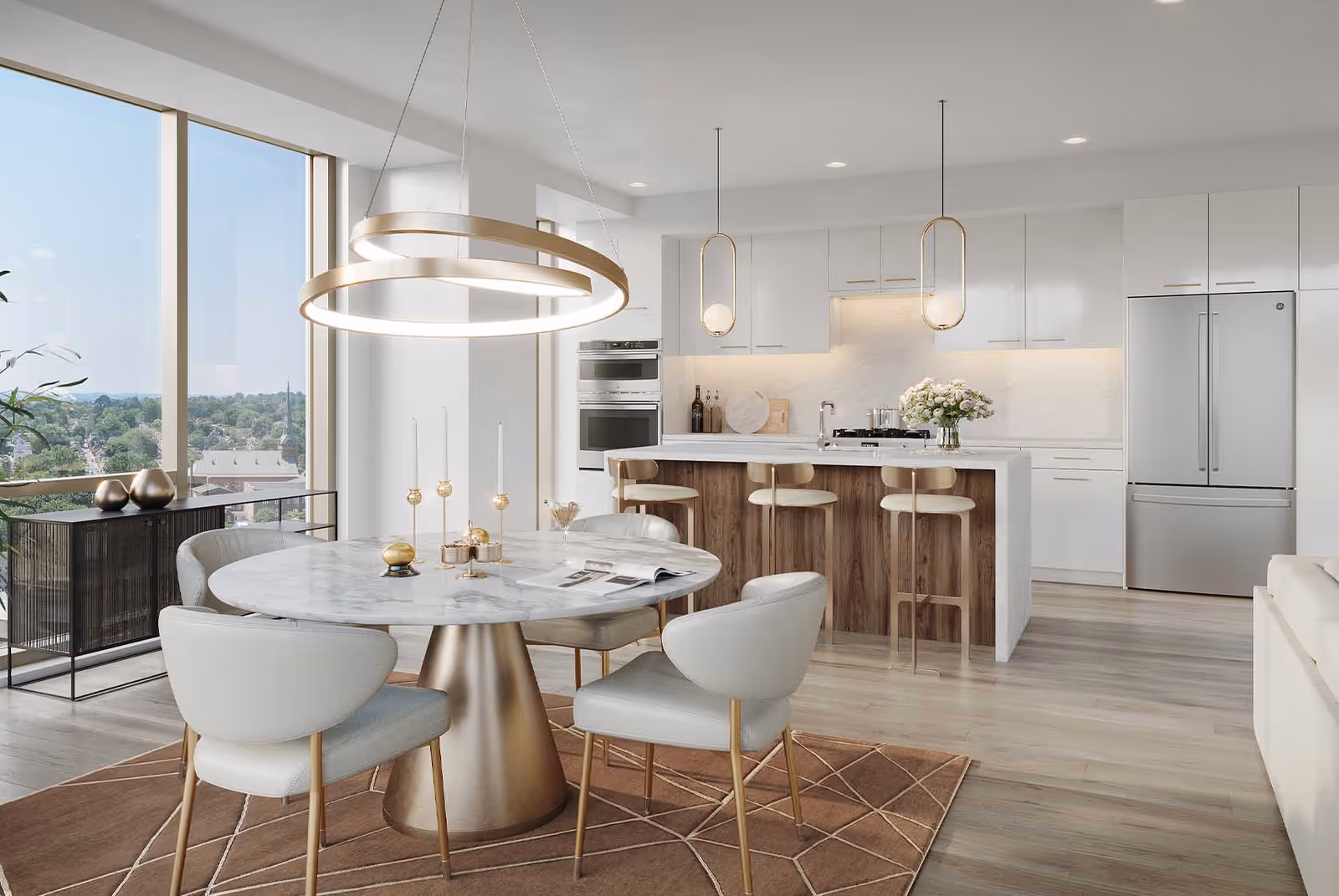 Modern open-concept kitchen and dining area with large windows offering a scenic view. The dining area features a round marble table with four upholstered chairs on a brown geometric rug. The kitchen has white cabinetry, a marble island with three wooden bar stools, stainless steel appliances, and pendant lighting above the island.