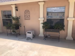 Exterior front view of Serenity House with columns, a window, and planters on wheeled stands along a concrete walkway.