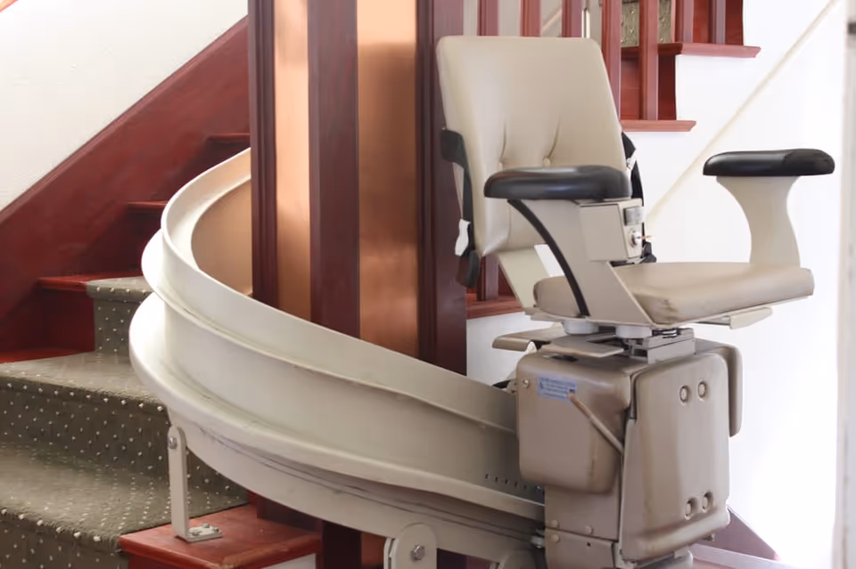 A beige stairlift chair mounted on a curved indoor staircase with wooden railings.