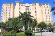 Front view of a multi-story beige residential building with palm trees and parked cars in the foreground.