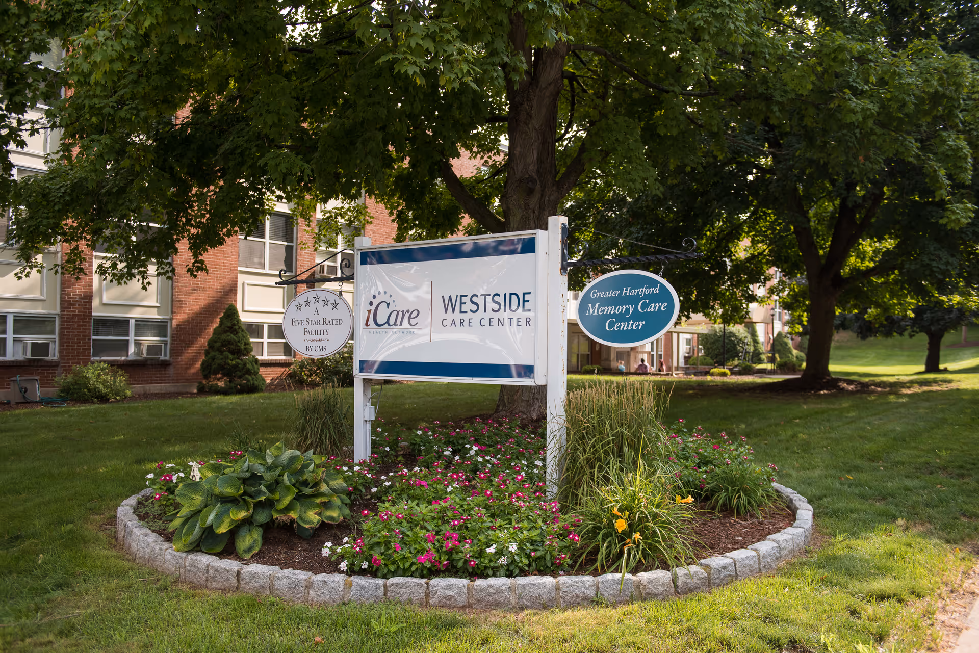 Landscaped entrance sign for Westside Care Center in front of a brick building surrounded by trees and flowers.