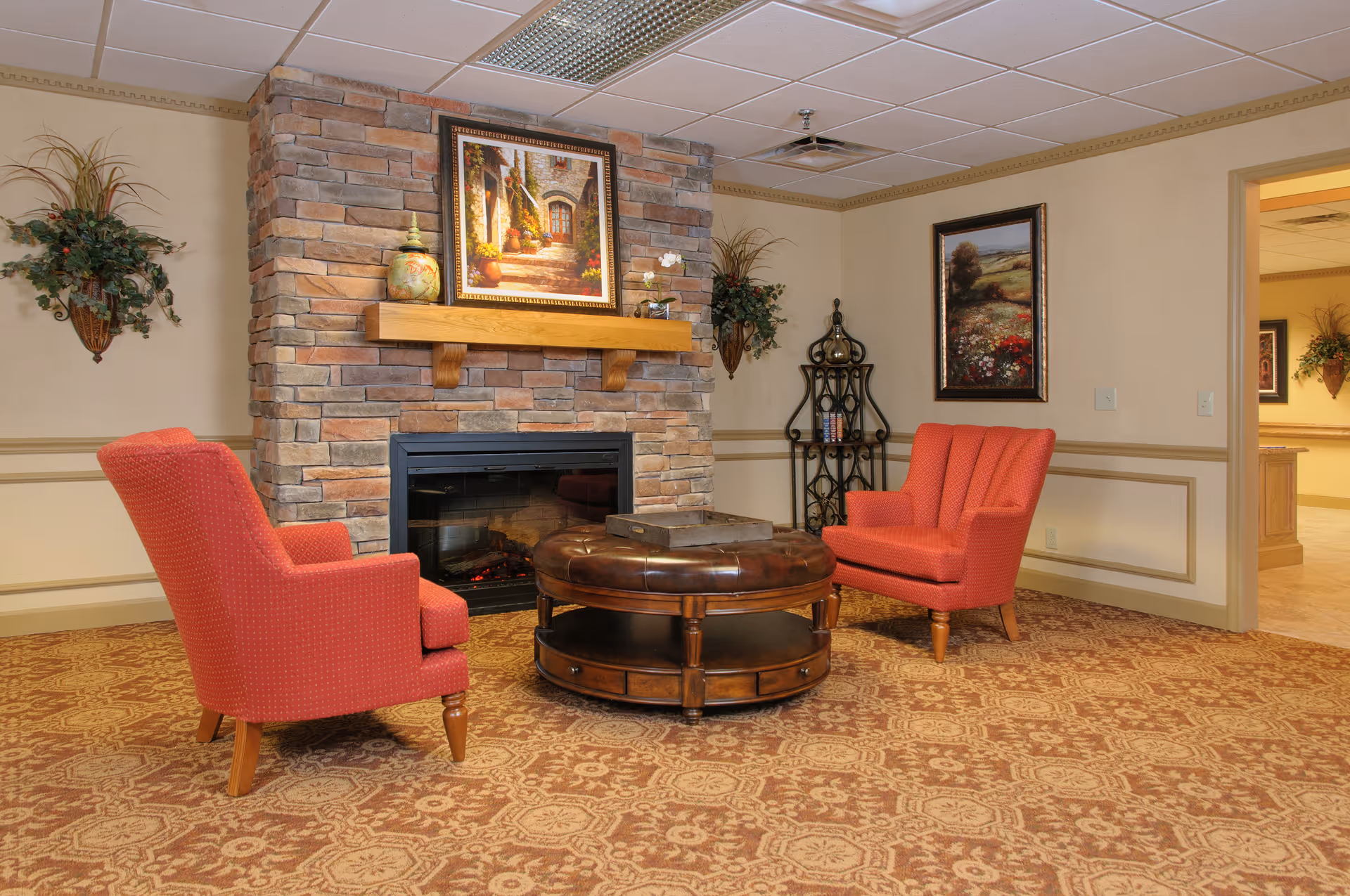 Cozy sitting area with two red armchairs facing a stone fireplace and round coffee table in a common room.