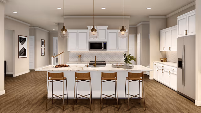 Modern kitchen interior with a large white marble island featuring four wooden bar stools. The kitchen has white cabinets, stainless steel appliances including a refrigerator and microwave, pendant lights hanging above the island, and wooden flooring. There are decorative items on the island and framed artwork on the walls in the background.
