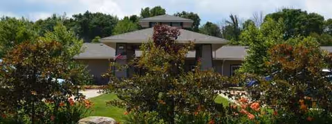 Exterior view of a senior living facility with landscaped trees and a walkway.